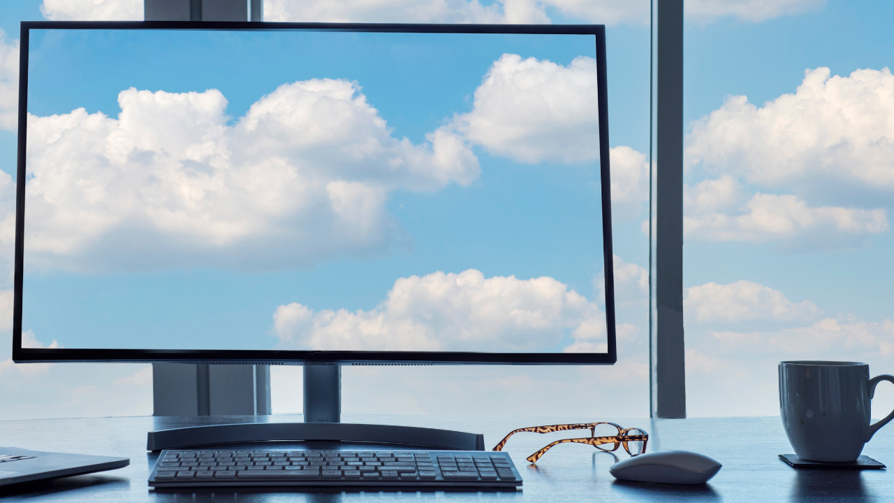 Picture of computer sitting on desk with a screensaver of a bright blue sky and clouds
