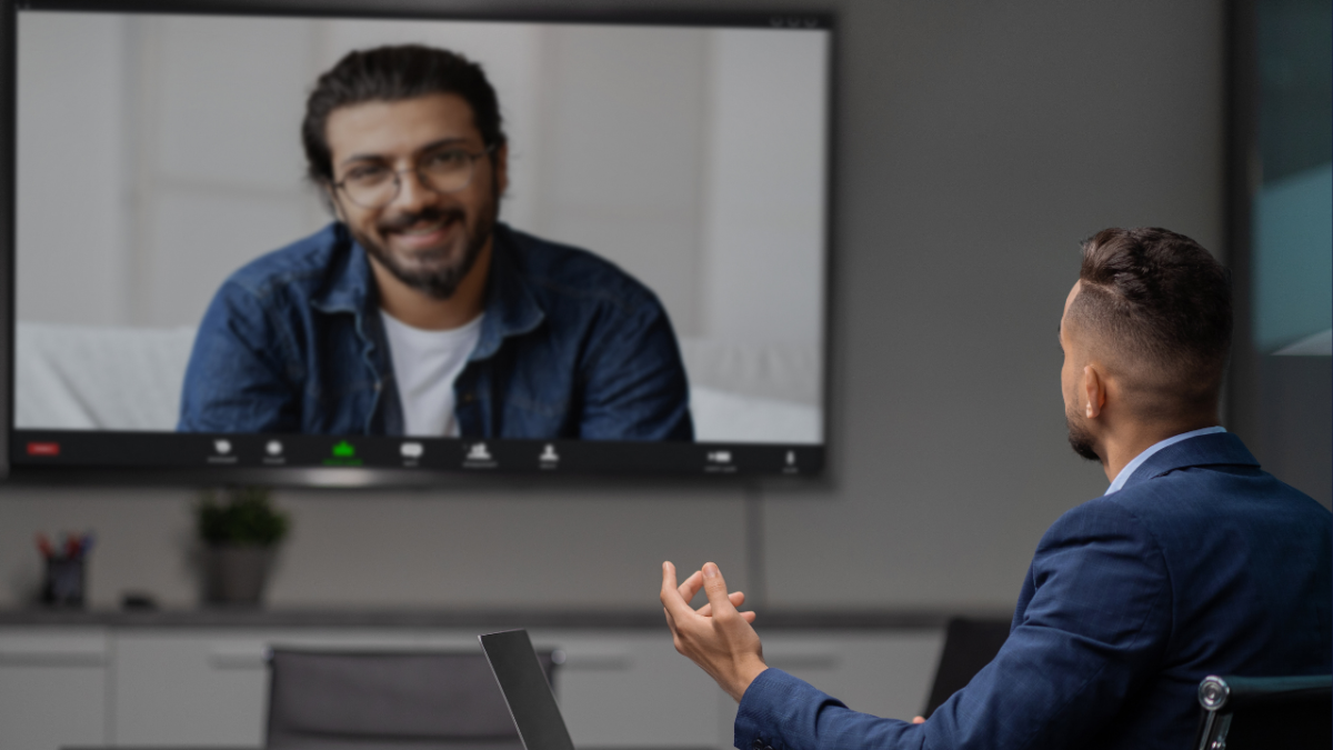 Business man in an office having a Zoom meeting with another business man on TV screen